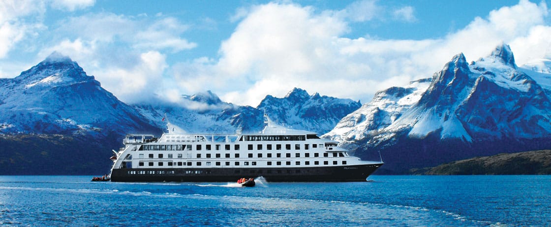 Un luxueux bateau de croisière navigue sur des eaux cristallines, entouré de montagnes majestueuses. TMR Voyages vous invite à explorer.