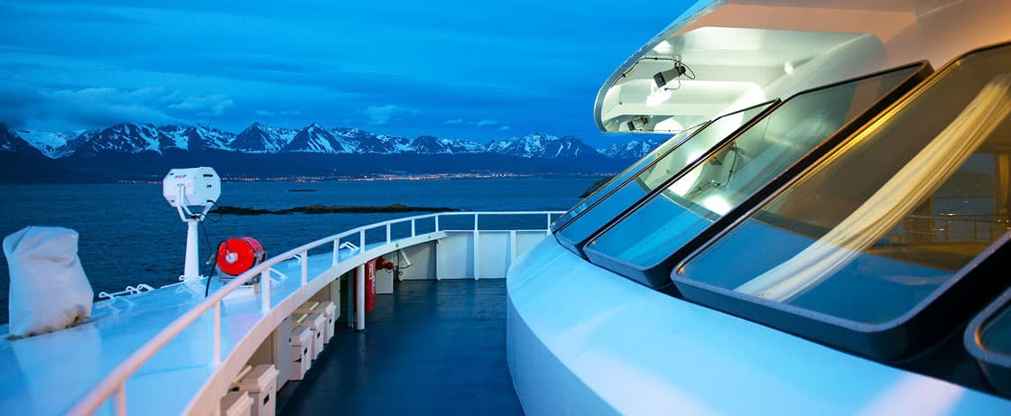 À bord d'un yacht de luxe, vue sur des montagnes majestueuses sous un ciel crépusculaire, un voyage d'exception avec TMR Voyages.