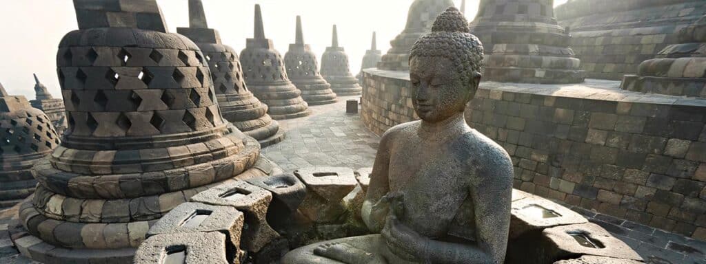 Bouddha en pierre au temple de Borobudur, symbole des découvertes culturelles en Indonésie. TMR Voyages pour une expérience authentique.