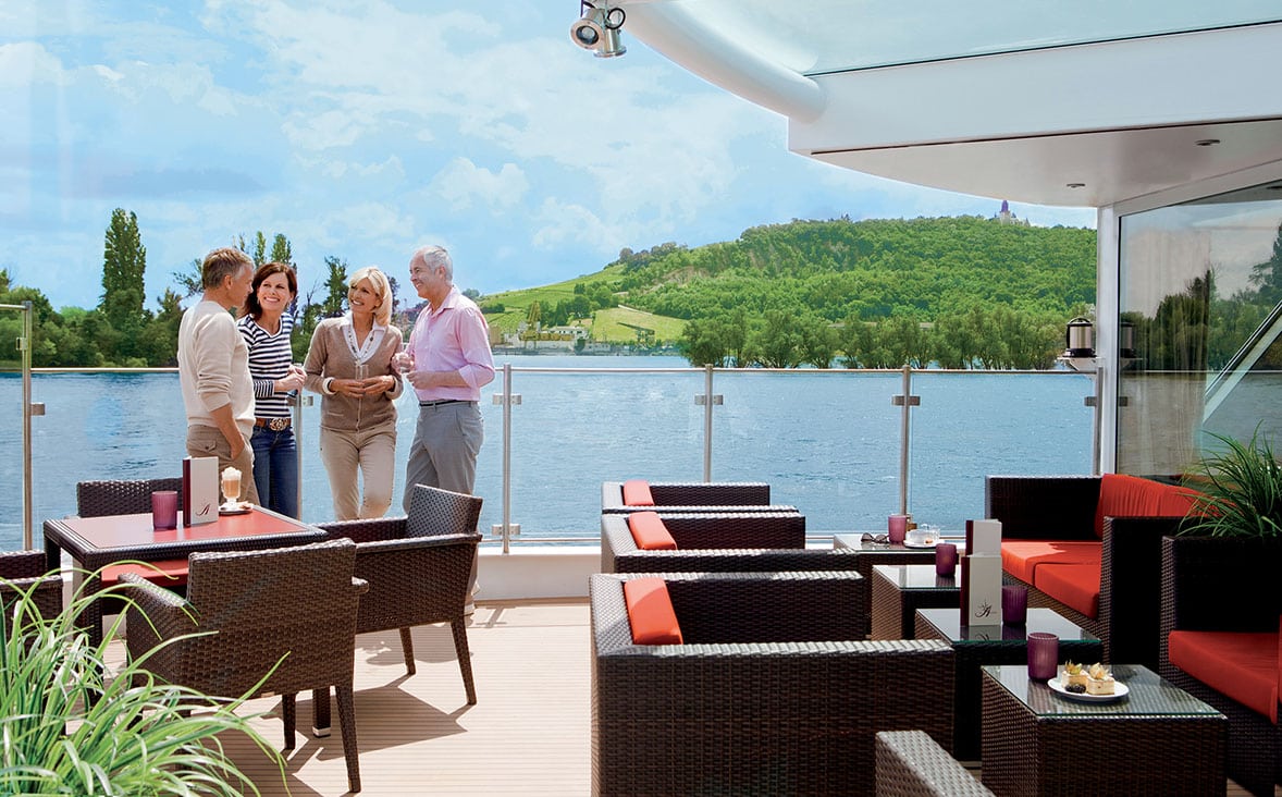 Sur le balcon d'un bateau, quatre personnes discutent, admirant un paysage verdoyant, le tout orchestré par TMR Voyages.