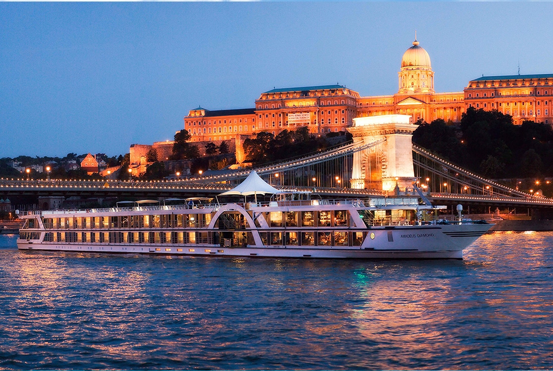 Un bateau de croisière de luxe navigue sous le pont en décoration lumineuse, avec le château en arrière-plan. TMR Voyages.