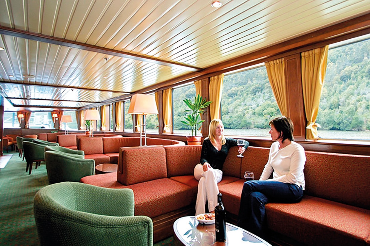 Dans un salon élégant, deux femmes partagent un verre face à une vue magnifique, une expérience de croisière de luxe avec TMR Voyages.