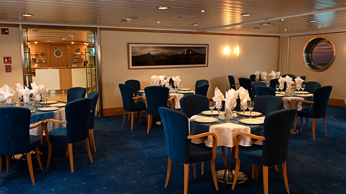 Une salle à manger élégante sur un bateau avec des tables impeccablement dressées, idéale pour un voyage de luxe avec TMR Voyages.