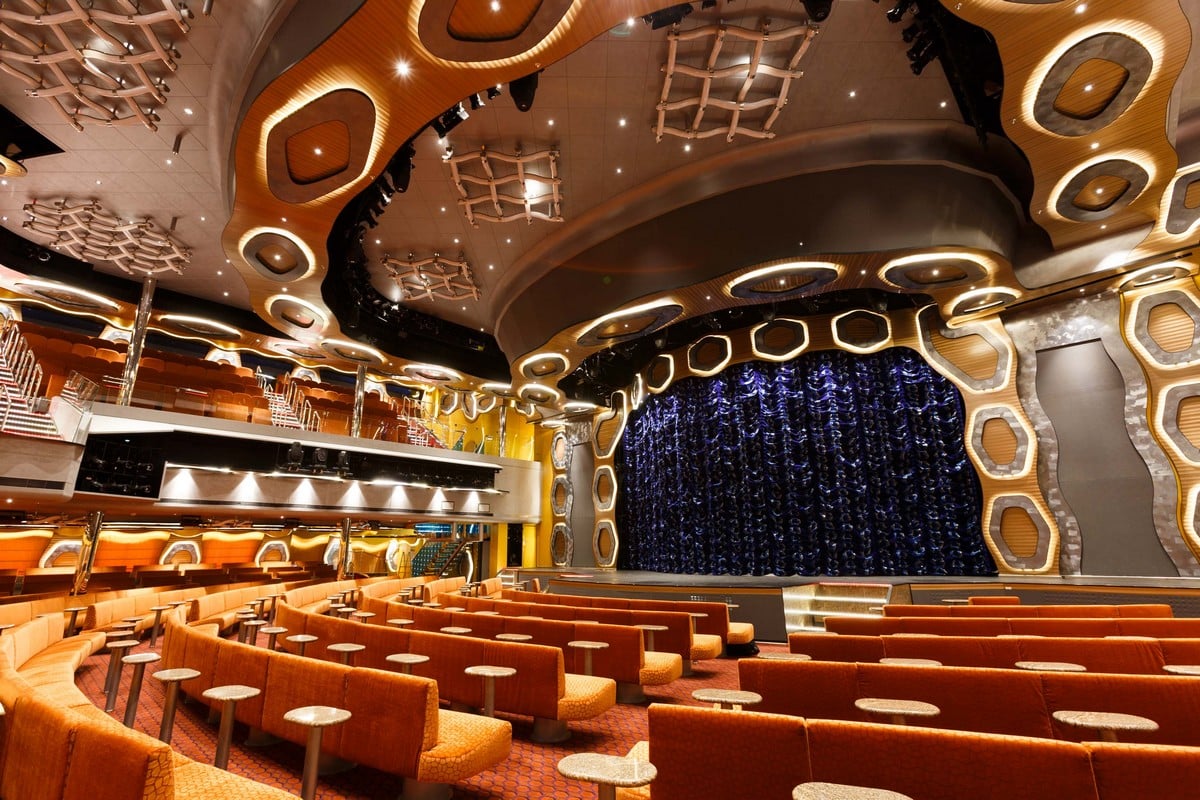 Un élégant auditorium avec des sièges orange et un rideau bleu, parfait pour une croisière de luxe avec TMR Voyages.