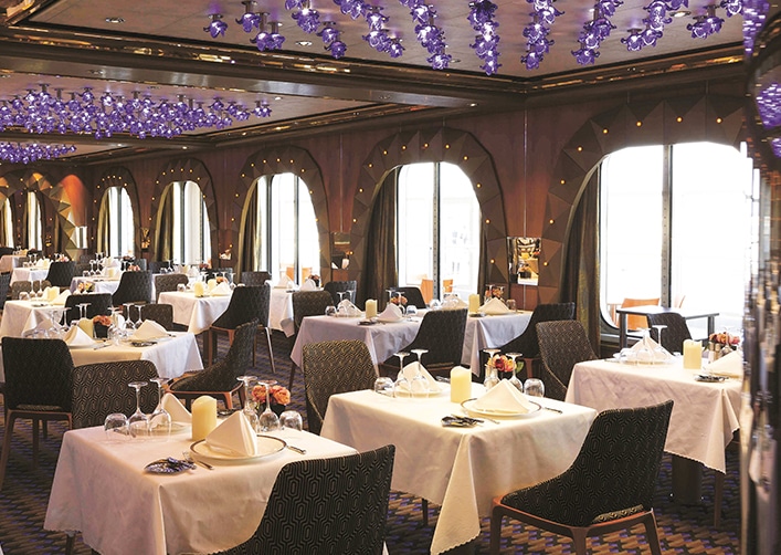 Un élégant restaurant avec tables napées et lampes violettes, parfait pour un voyage d’exception avec TMR Voyages.