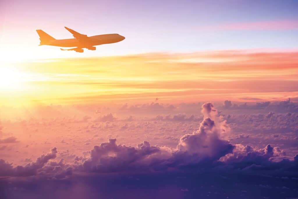 Un avion survole des nuages colorés au coucher du soleil, symbolisant des voyages d'aventure et des expériences authentiques avec TMR Voyages.