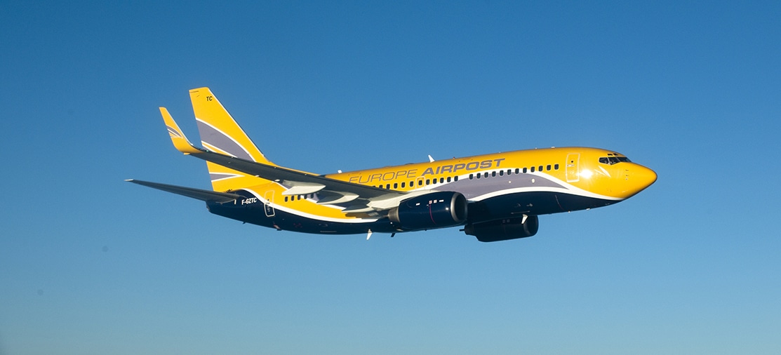 Un avion Europe Airpost survole un ciel bleu limpide, parfait pour un voyage d’exception avec TMR Voyages.