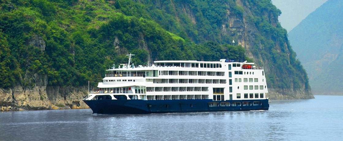 Un élégant bateau de croisière sur une rivière bordée de falaises verdoyantes, une expérience signée TMR Voyages.
